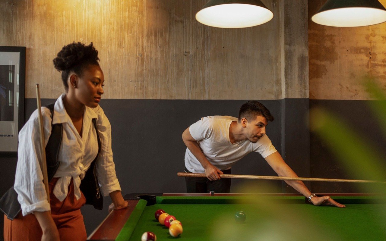 Symbolbild Billard/Darts: Zwei Freunde spielen Billard bei warmem Licht in einer Bar