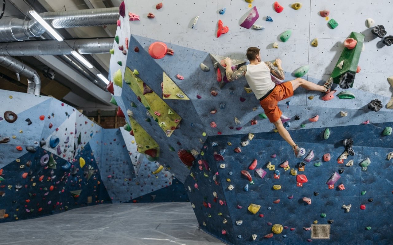 Symbolbild Bouldern/Klettern: Mann bouldert an bunter Wand in heller Kletterhalle