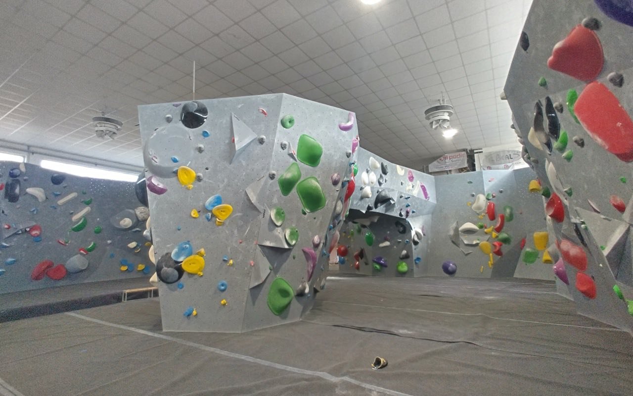 Symbolbild Bouldern/Klettern: Leere Boulderhalle mit grauen Wänden und bunten Griffen