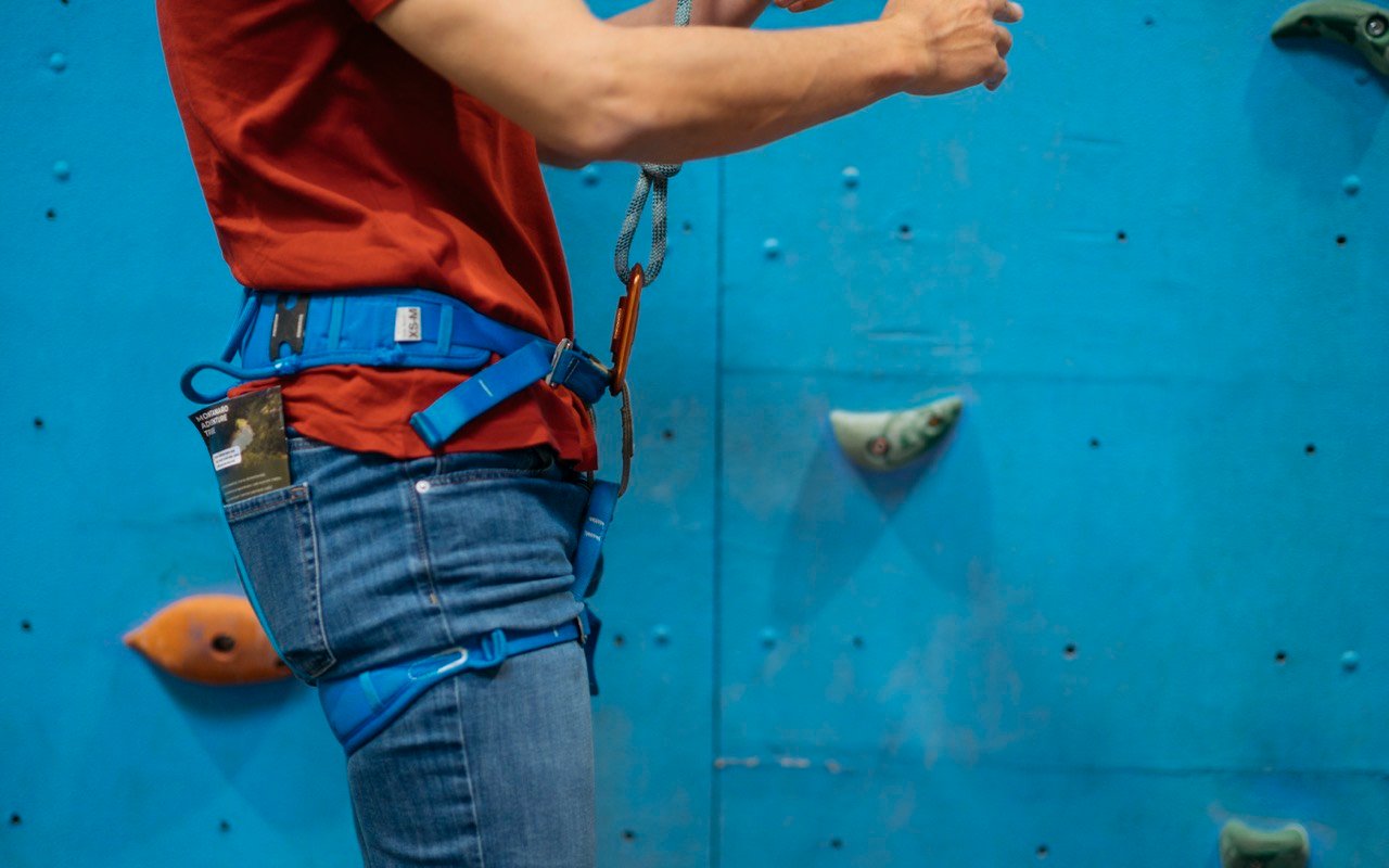 Symbolbild Bouldern/Klettern: Kletterer mit Gurt an einer blauen Wand