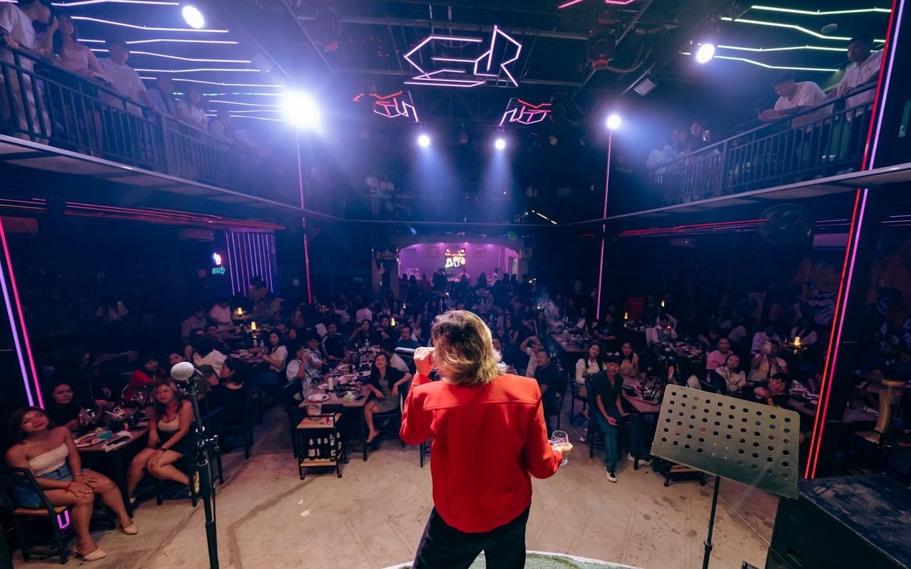 Symbolbild Kabarett/Comedy: Künstlerin auf Bühne vor vollem Saal mit Publikum an Tischen