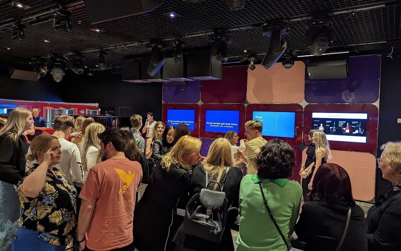Symbolbild Karaoke: Gäste von hinten vor einer Wand mit Karaoke Bildschirmen in einem Club