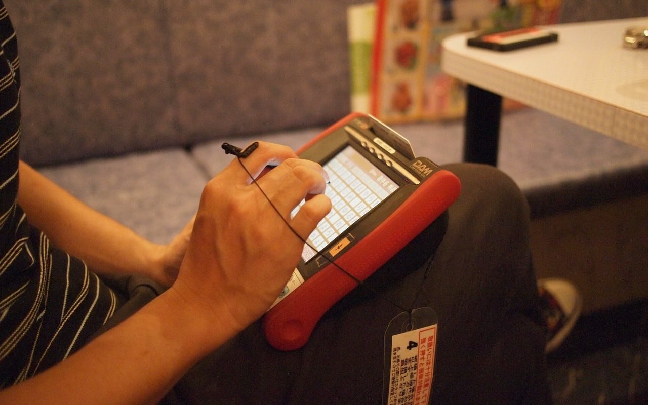 Symbolbild Karaoke: Hand wählt mit einem Stift auf einem Touchgerät ein Lied im Karaokeraum